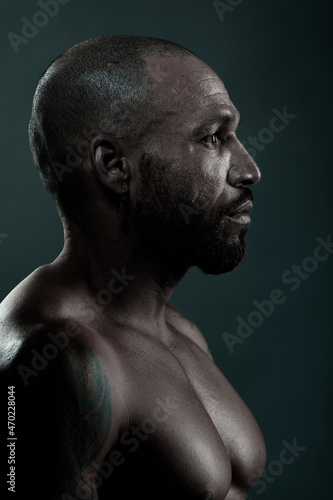 Male studio portrait close-up. Swarthy Cuban or Latino with naked muscular body looks away. Side view in profile. Brutal face.