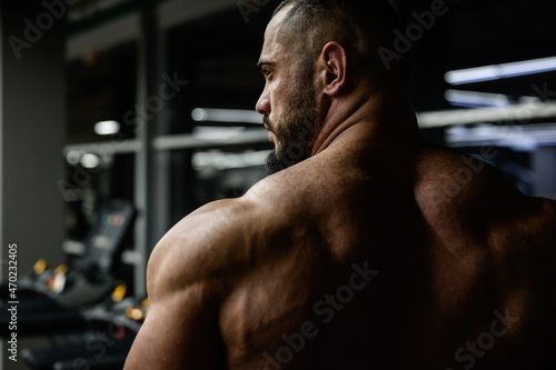 strong young bearded male trainer with muscular back shoulders in night sport fitness gym