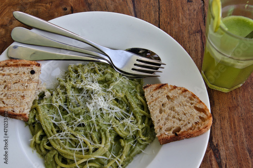 Close up of spaghetti pasta in pesto sauce with toasted bread, mint lemonade and stainless steel cutlery