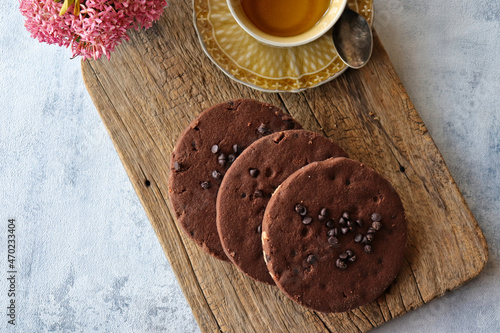 Chocolate chip cookies with a cup of black tea on a wooden board with pink flowers