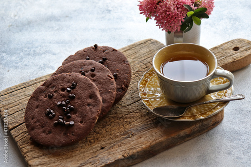 Chocolate chip cookies with a cup of black tea on a wooden board with pink flowers