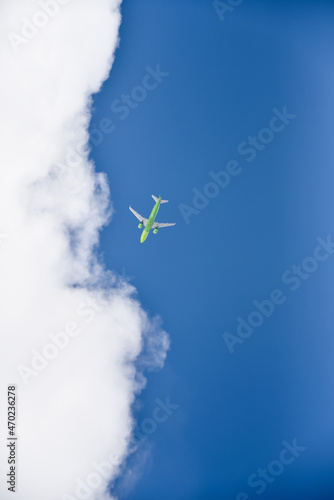 The low-angle shot of a passenger plane with a green body with clouds and blue sky background