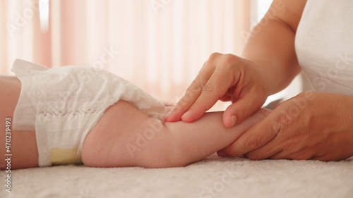 Mother doing massage for her healthy infant baby. Small caucasian newborn laying on his belly while his mother is performing a massage for his small feet and developing toes. .