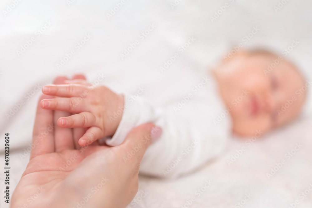 Young woman holding small hand of her sleeping baby daughter in bedroom Young woman holding small hand of her sleeping baby daughter in bedroom