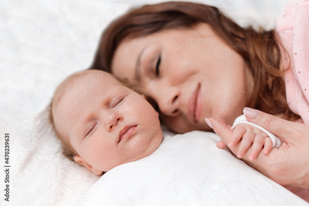Young beautiful woman holding small hand of her sleeping baby daughter in bedroom Young beautiful woman holding small hand of her sleeping baby daughter in bedroom