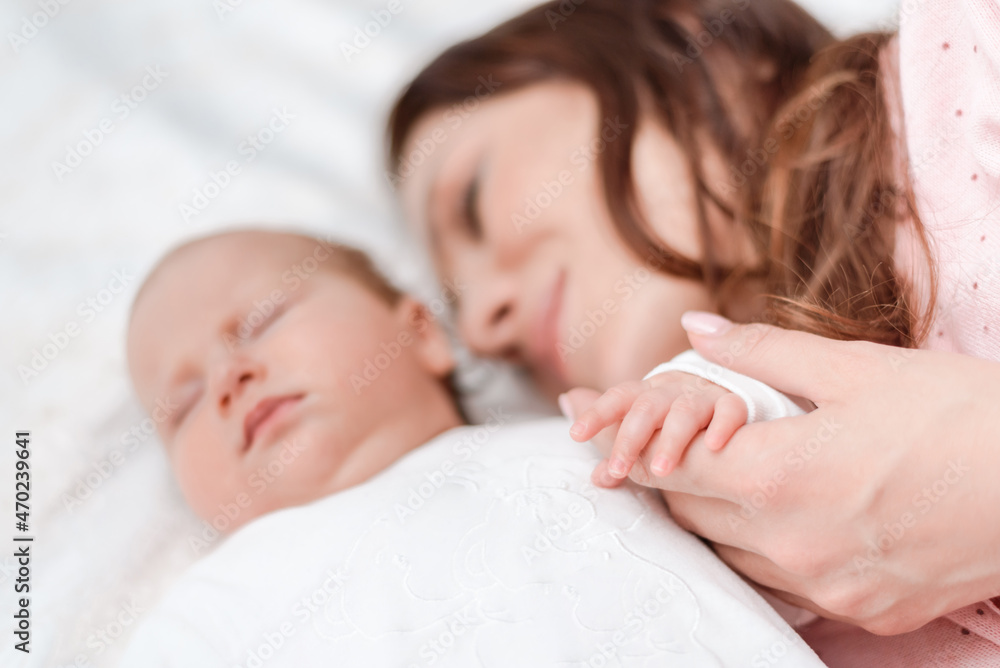 Young beautiful woman holding small hand of her sleeping baby daughter in bedroom Young beautiful woman holding small hand of her sleeping baby daughter in bedroom