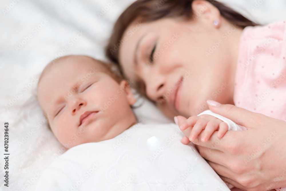 Young beautiful woman holding small hand of her sleeping baby daughter in bedroom Young beautiful woman holding small hand of her sleeping baby daughter in bedroom