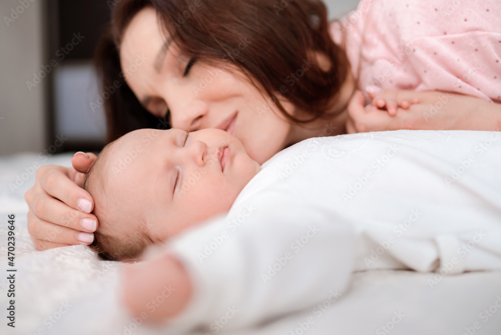 Young woman lovingly looks at her sleeping newborn daughter in the bedroom Young woman lovingly looks at her sleeping newborn daughter in the bedroom