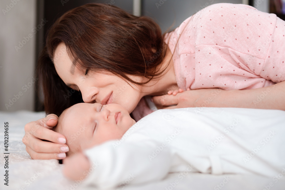 Young woman lovingly looks at her sleeping newborn daughter in the bedroom Young woman lovingly looks at her sleeping newborn daughter in the bedroom