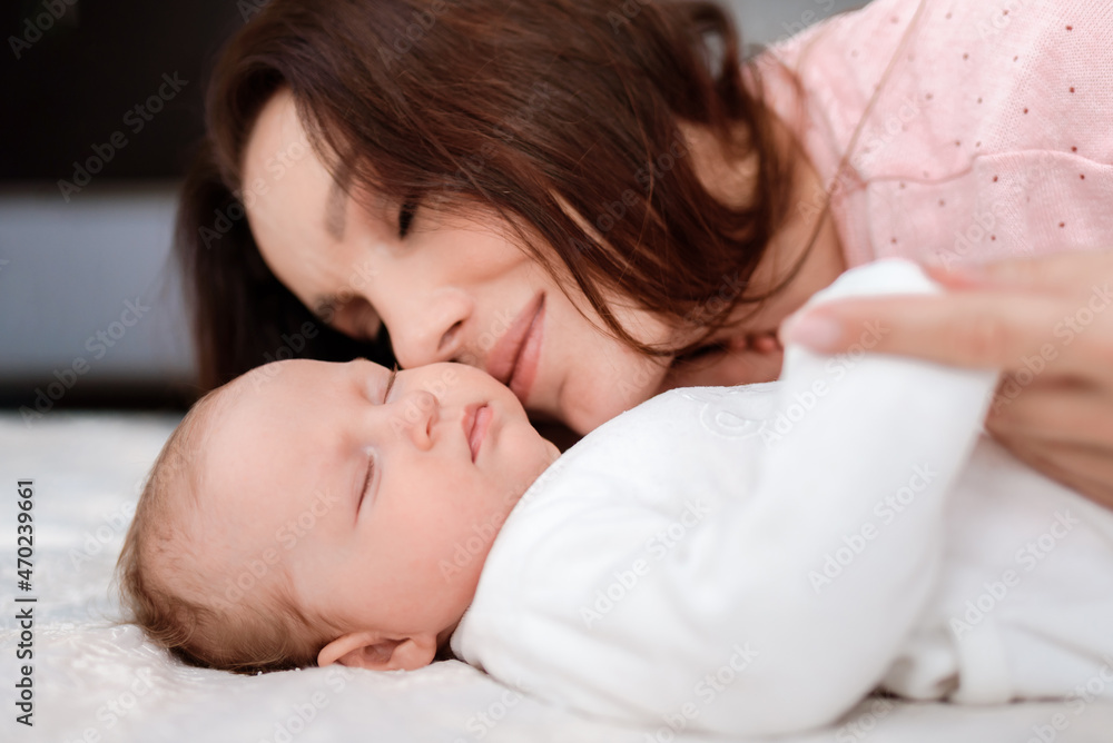 Young woman lovingly looks at her sleeping newborn daughter in the bedroom Young woman lovingly looks at her sleeping newborn daughter in the bedroom