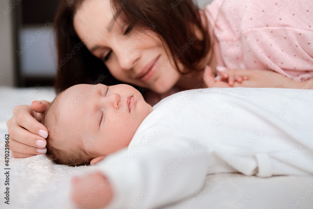 Young woman lovingly looks at her sleeping newborn daughter in the bedroom Young woman lovingly looks at her sleeping newborn daughter in the bedroom