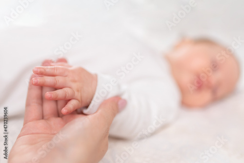 Young woman holding small hand of her sleeping baby daughter in bedroom