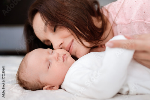Young woman lovingly looks at her sleeping newborn daughter in the bedroom