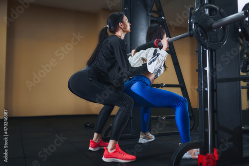 Young brunette woman working out legs with barbell in gym. personal female trainer. Squat Exercise 