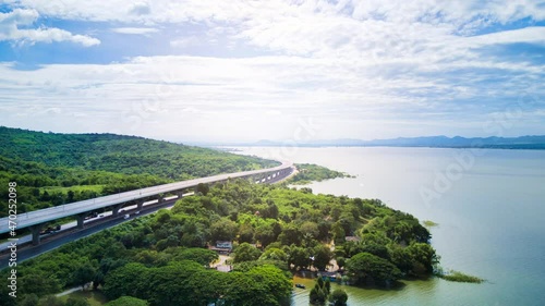 Aerial drone hyper lapse time lapse of beautiful expressway in a green forest with a dam on the side of the road between mountains.	