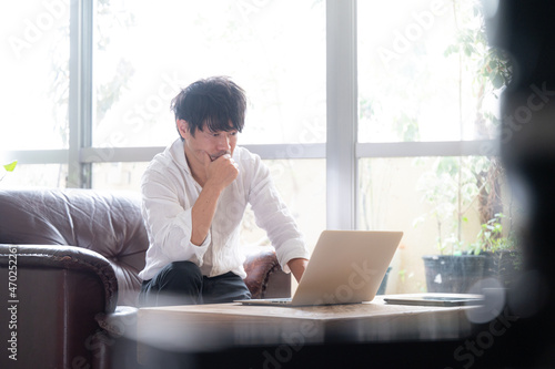 白くて広いリビングで仕事をする日本人（アジア人）ビジネスマンの男性 コピースペースあり 前ボケあり