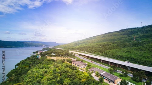 Aerial drone hyper lapse time lapse of beautiful expressway in a green forest with a dam on the side of the road between mountains.