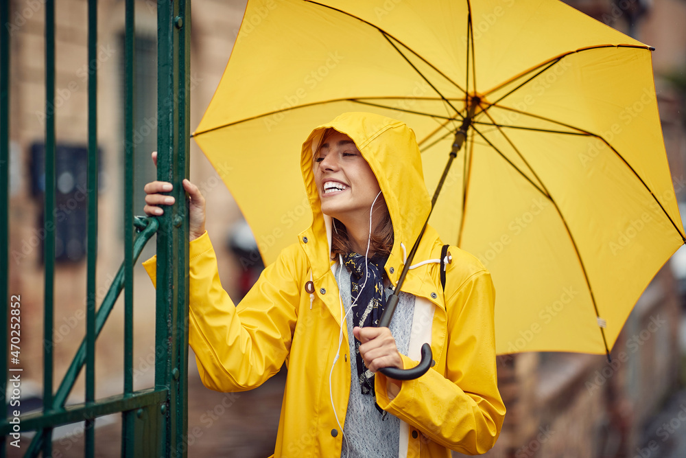 Close-up of a young girl with yellow raincoat and umbrella who likes to walk the city on the rain. Walk, rain, city - obrazy, fototapety, plakaty 