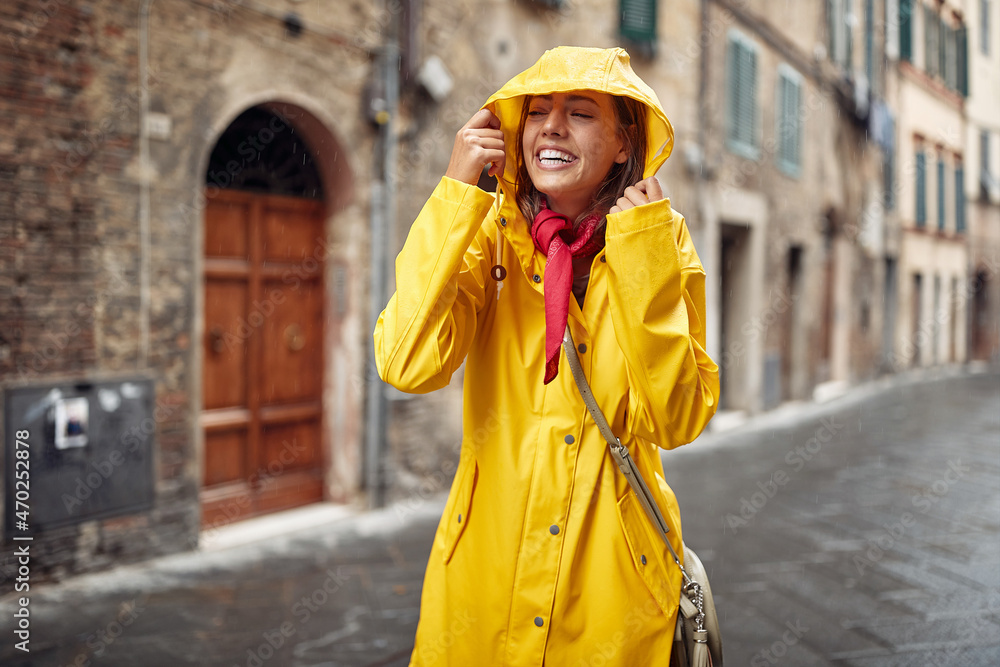 Fototapeta premium A young girl in a yellow raincoat walks on the street during a rain. Walk, rain, city. Walk, rain, city