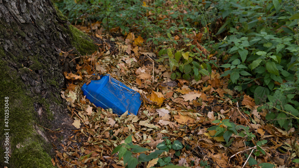 Obraz premium Environmental pollution. An old blue plastic canister from gasoline lies in the forest by a tree among the leaves. Toxicity. Soil contamination with hydrocarbons. Ecology.