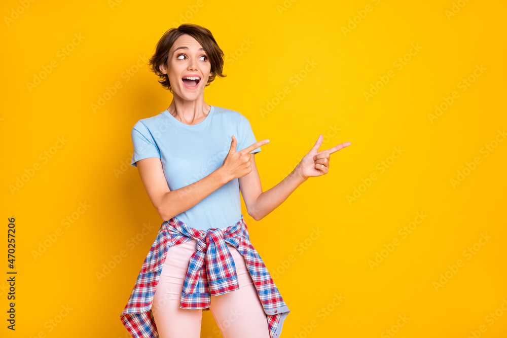 Photo portrait of excited woman looking pointing two fingers at blank space with shirt on waist isolated on vivid yellow colored background
