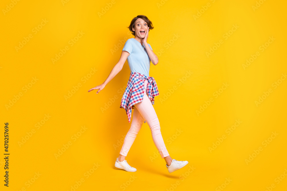 Full length profile photo portrait of impressed woman walking with tight waist shirt isolated on vivid yellow colored background Full length profile photo portrait of impressed woman walking with tight waist shirt isolated on vivid yellow colored background