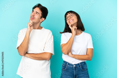 Young mixed race couple isolated on blue background thinking an idea while looking up