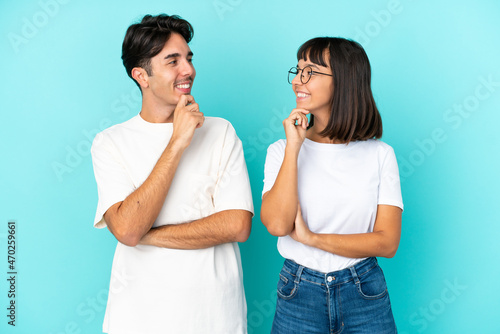 Young mixed race couple isolated on blue background looking looking at each other