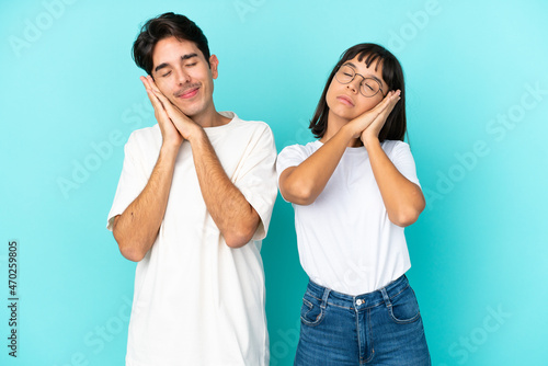 Young mixed race couple isolated on blue background making sleep gesture in dorable expression