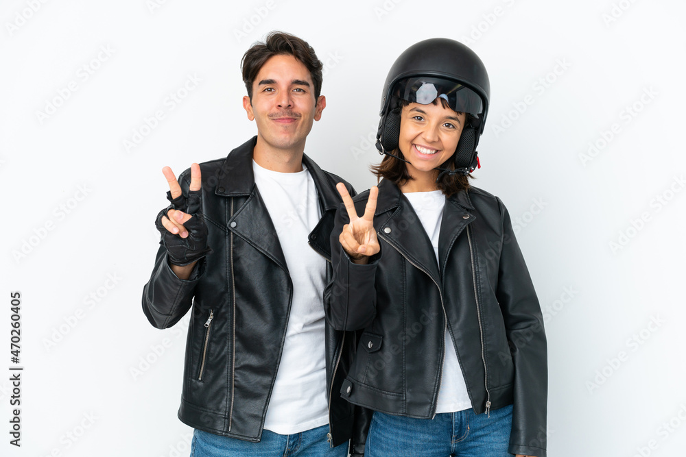 Young mixed race couple with a motorcycle helmet isolated on white background smiling and showing victory sign Young mixed race couple with a motorcycle helmet isolated on white background smiling and showing victory sign