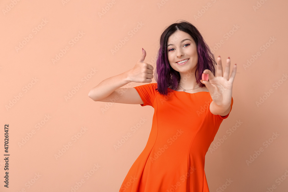 Young woman with pink chewing gum showing thumb-up on beige background Young woman with pink chewing gum showing thumb-up on beige background