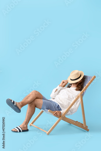 Valokuva Handsome young man sitting on deck chair against color background