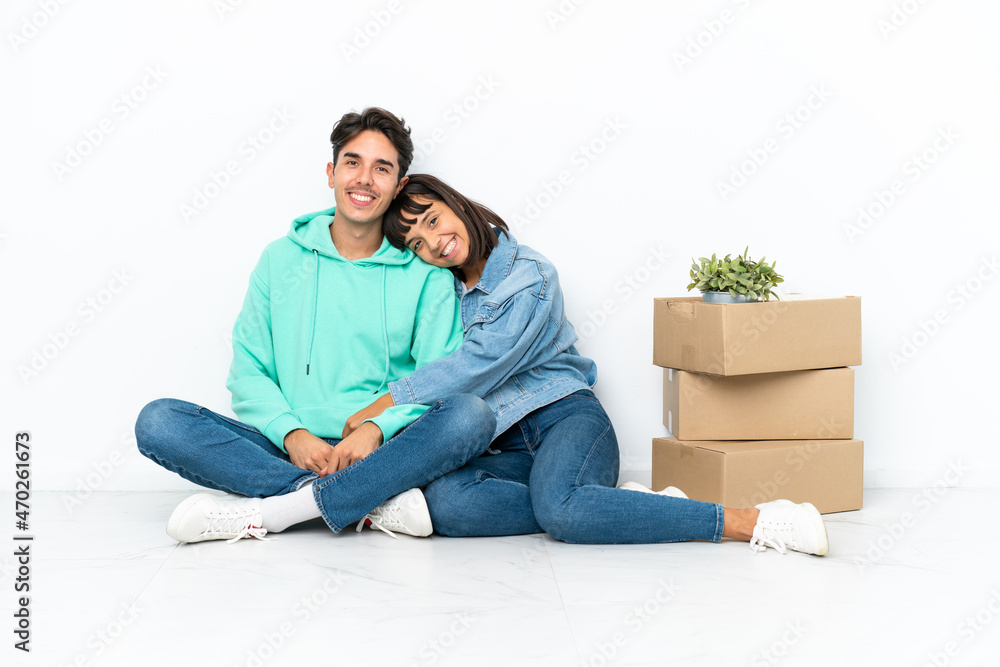 Young couple making a move while picking up a box full of things sitting on the floor isolated on white background keeping the arms crossed in frontal position Young couple making a move while picking up a box full of things sitting on the floor isolated on white background keeping the arms crossed in frontal position