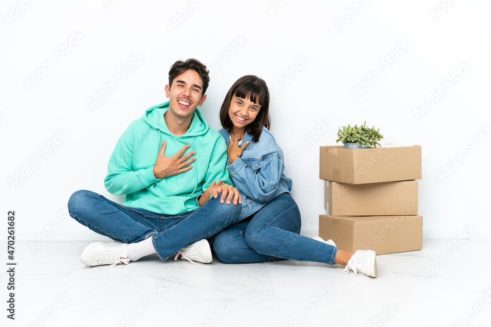 Young couple making a move while picking up a box full of things sitting on the floor isolated on white background keeping the arms crossed while smiling Young couple making a move while picking up a box full of things sitting on the floor isolated on white background keeping the arms crossed while smiling