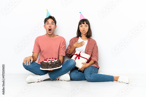 Foto Young mixed race couple celebrating a birthday sitting on the floor isolated on