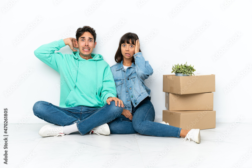 Young couple making a move while picking up a box full of things sitting on the floor isolated on white background takes hands on head because has migraine Young couple making a move while picking up a box full of things sitting on the floor isolated on white background takes hands on head because has migraine