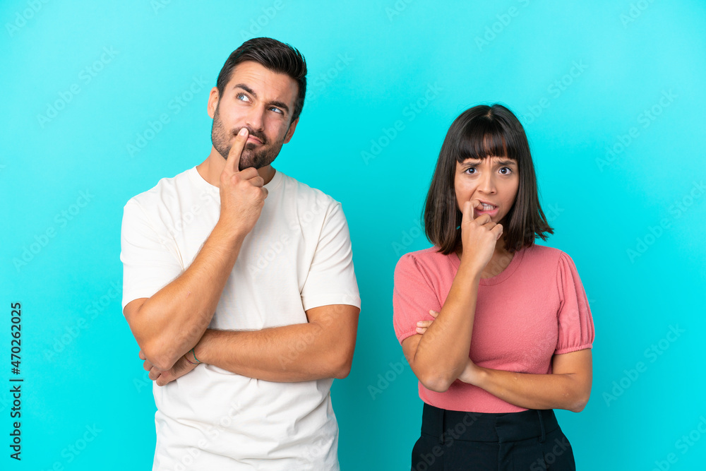 Young couple isolated on blue background having doubts while looking up Young couple isolated on blue background having doubts while looking up