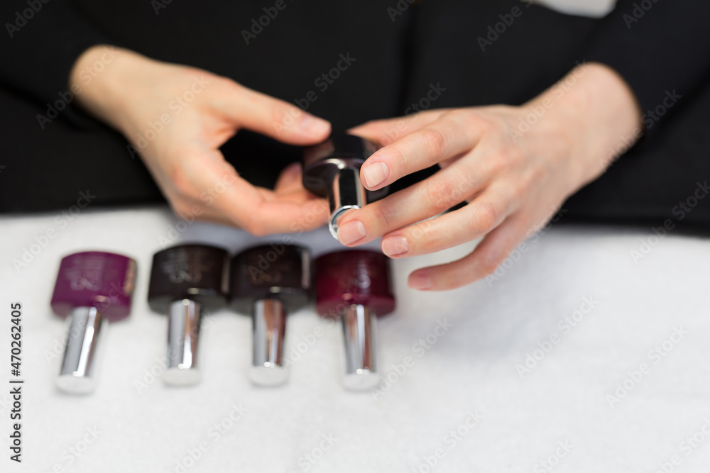Fototapeta premium Manicure and nail care concept. A woman in a beauty salon holds colored test nail polishes with different colors and chooses the color for painting.
