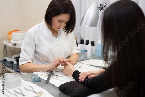 Manicurist doing hardware manicure to a young beautiful girl in the spa salon. Hardware manicure. Concept of body care