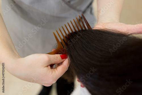 Strong, shiny and healthy long brunette hair. Hairdresser combing the hair of the client. Close-up of beautiful silky hair is in hands of stylist