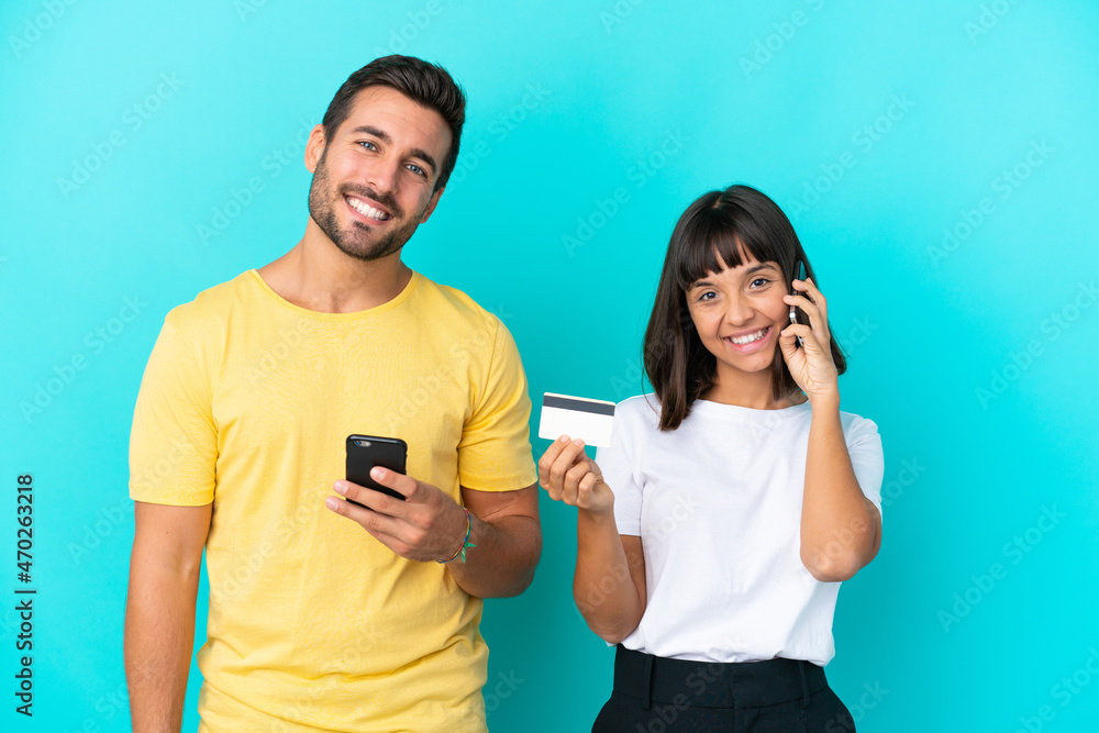 Young couple isolated on blue background keeping a conversation with the mobile phone and holding a credit card Young couple isolated on blue background keeping a conversation with the mobile phone and holding a credit card