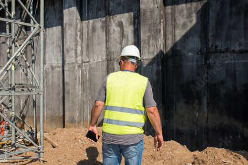 Foreman in a safety helmet and a vest with a telephone at a construction site