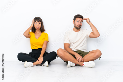 Young couple sitting on the floor isolated on white background with an expression of frustration and not understanding