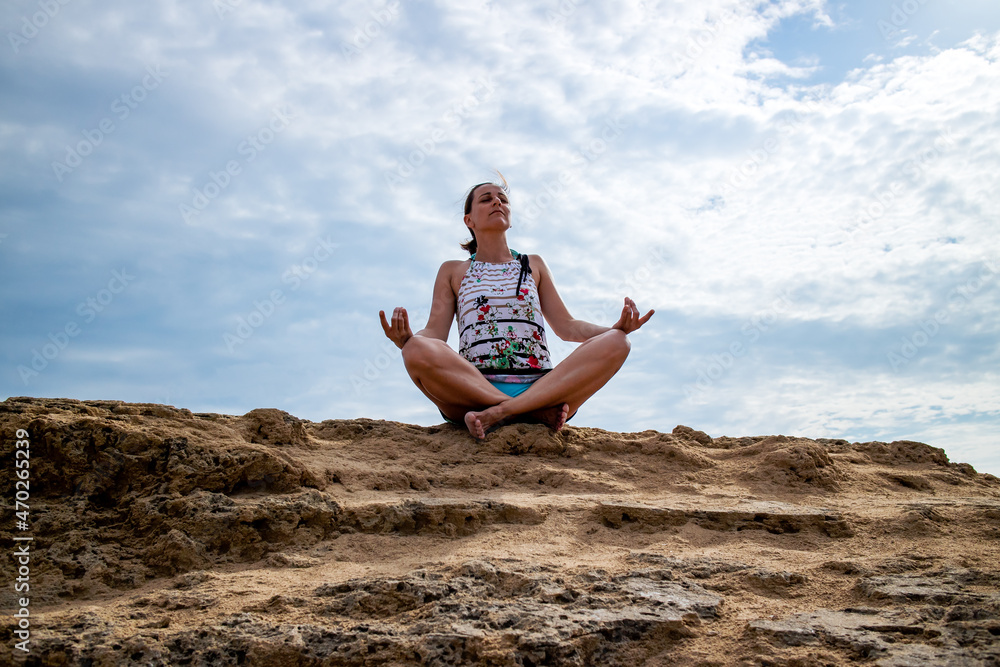 Woman meditating in lotus pose, sitting on the sandy rock, relaxing and enjoying in silence and peace.
