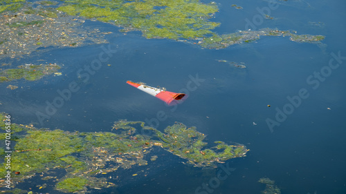 An orange traffic cone floating in a eutrophic river water after being thrown in photo
