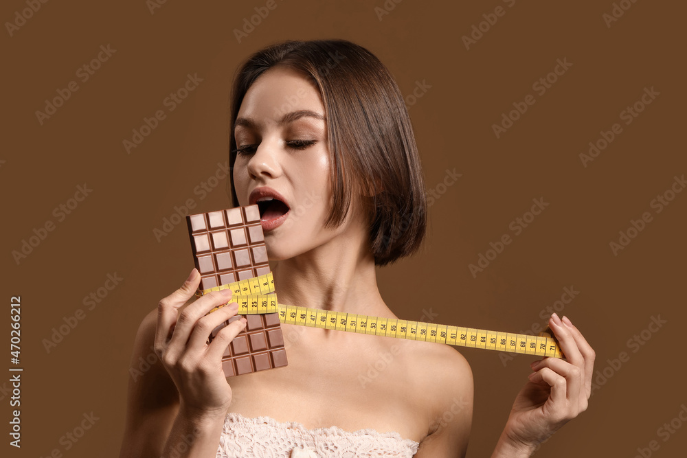 Beautiful young woman with sweet chocolate and measuring tape on color background. Diet concept