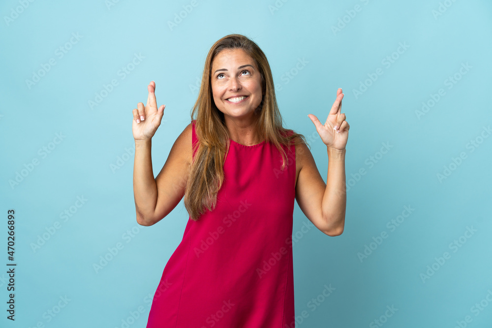 Middle age brazilian woman isolated on blue background with fingers crossing Middle age brazilian woman isolated on blue background with fingers crossing