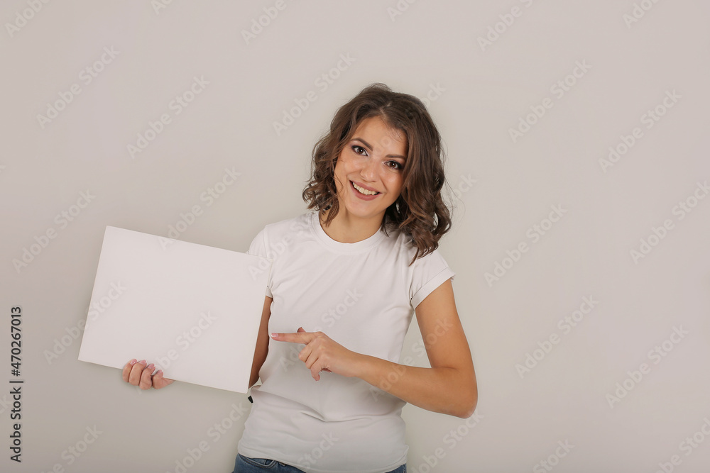 a young beautiful brown-haired girl in a white T-shirt holds a white sheet of paper in her hands