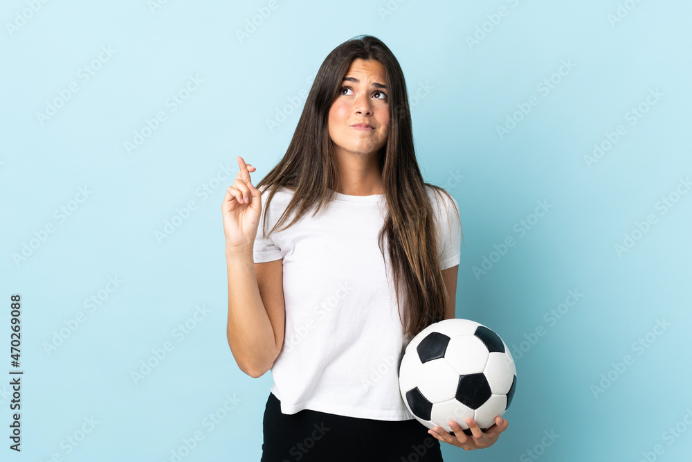 Young football player brazilian girl isolated on blue background with fingers crossing and wishing the best Young football player brazilian girl isolated on blue background with fingers crossing and wishing the best