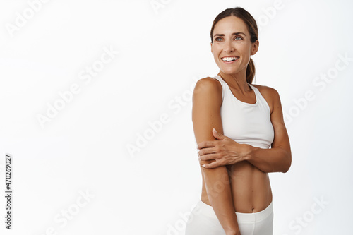 Middle aged 30 years old fitness woman with fit and strong body, abs and muscles, looking aside happy and smiling, exercise in gym, workout indoors, white background